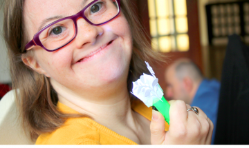 Uśmiechnięta dziewczyna z zespołem Downa trzyma w ręku ozdobioną ręcznie małą latareczkę. Na dole zdjęcia znajdują się logotypy Fundacji Ewangelickie Centrum Diakonii i Edukacji, Państwowego Funduszu Rehabilitacji Osób Niepełnosprawnych, Miejskiego Ośrodka Pomocy Społecznej we Wrocławiu i Biura Bez Barier.